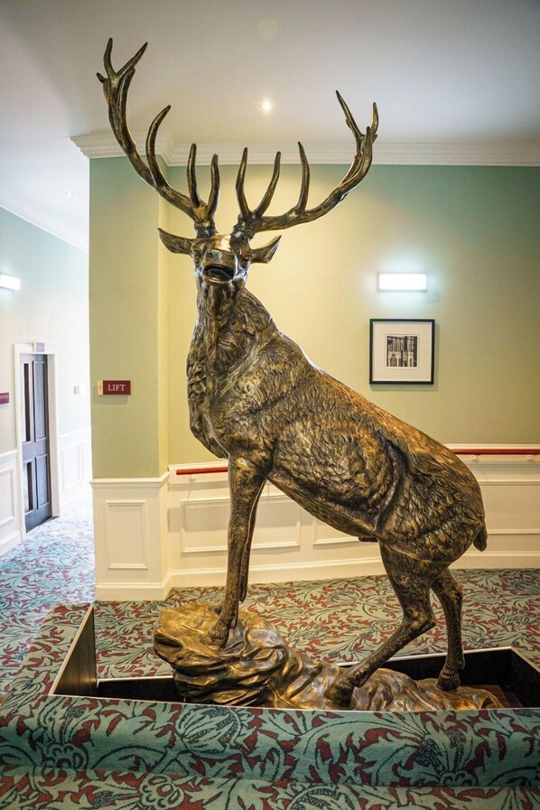 Une grande sculpture de cerf orne le hall, qui est décoré d’un tapis à motifs, d’un panneau indiquant l’emplacement de l’ascenseur et d’un tableau encadré accroché au mur.
