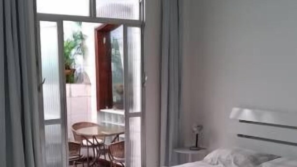 Ein Schlafzimmer mit Bett, einem kleinen Tisch und einem Sessel in der Nähe einer Glastür zu einem Außenbereich.