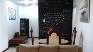 Ein Wohnzimmer mit einem beigen Sofa, einem Holzesstisch mit Stühlen, einer Tafel an der Wand und einer Deckenleuchte.