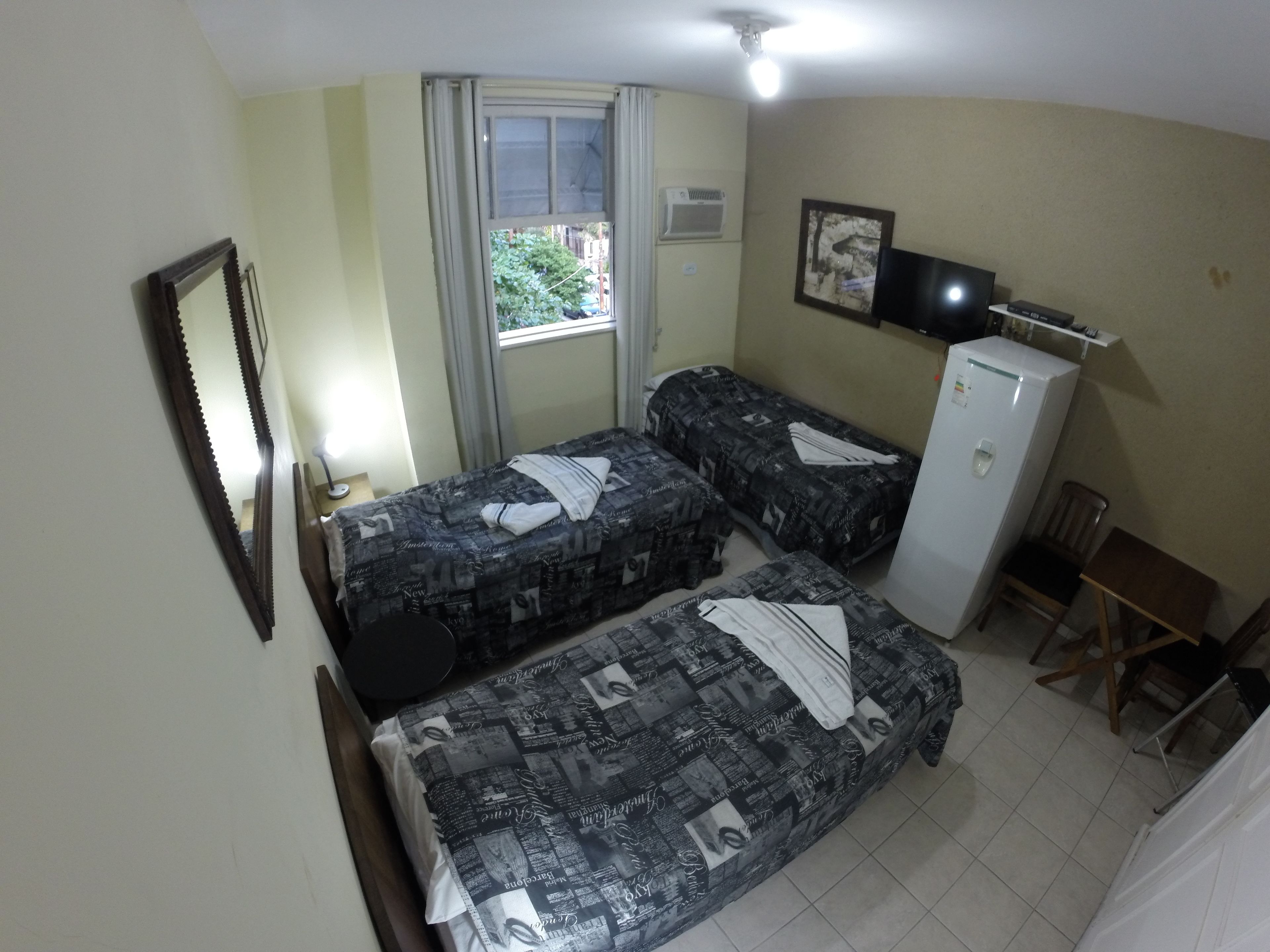 A small, compact room with two single beds, a desk, a chair, a TV, and a refrigerator.