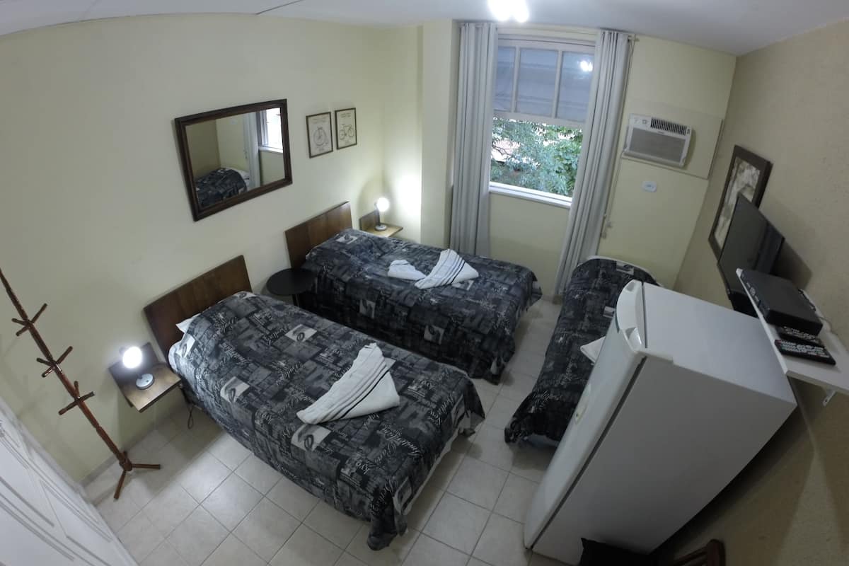 Ein Hotelzimmer mit zwei Betten, einem Schreibtisch, einem Stuhl, einem Spiegel, einem fenster mit Vorhängen und einer Klimaanlage.