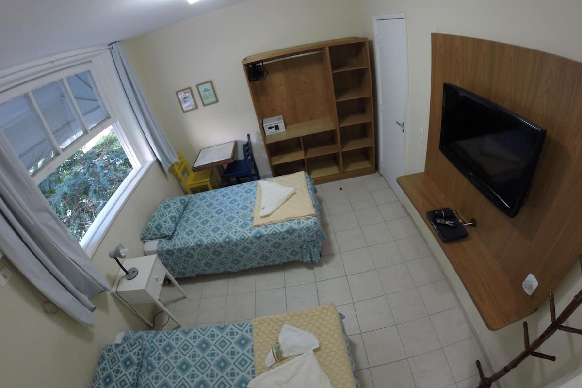 Ein kleines Zimmer mit zwei Betten, einem Fernseher, einem Schreibtisch und einem Kleiderschrank.