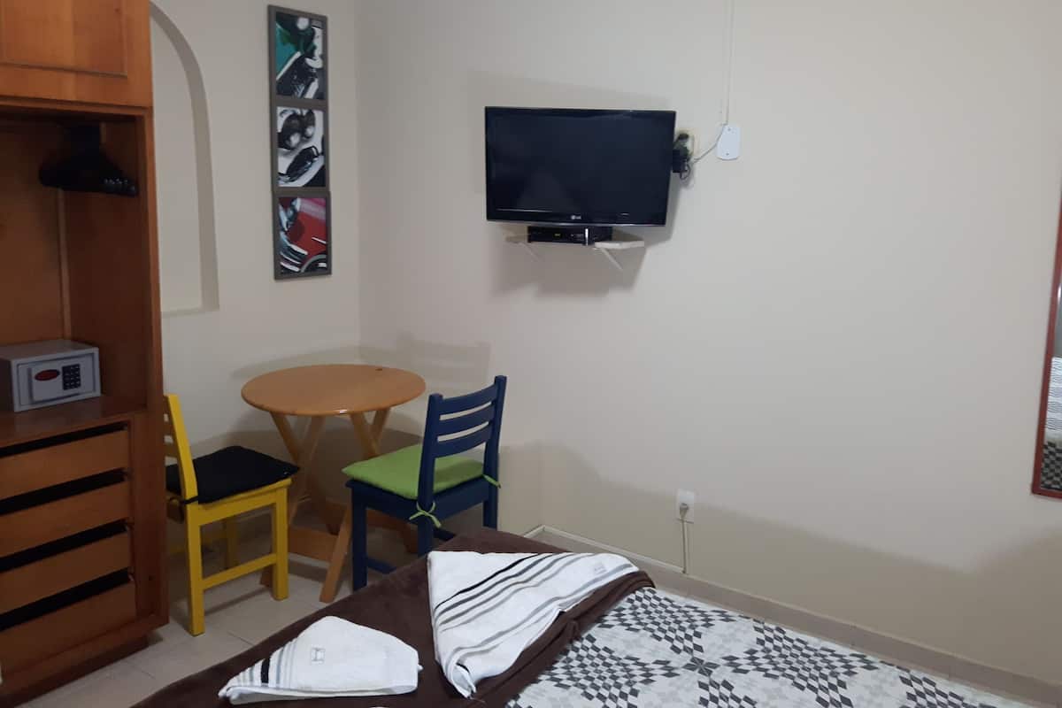 Ein Schlafzimmer mit einem Bett, einem an der Wand montierten Fernseher, einem kleinen runden Tisch und zwei Stühlen.