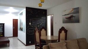 A living room with a dining area, a blackboard with writing, a painting, and a wooden door. - Margaridas Pousada (Rio de Janeiro)