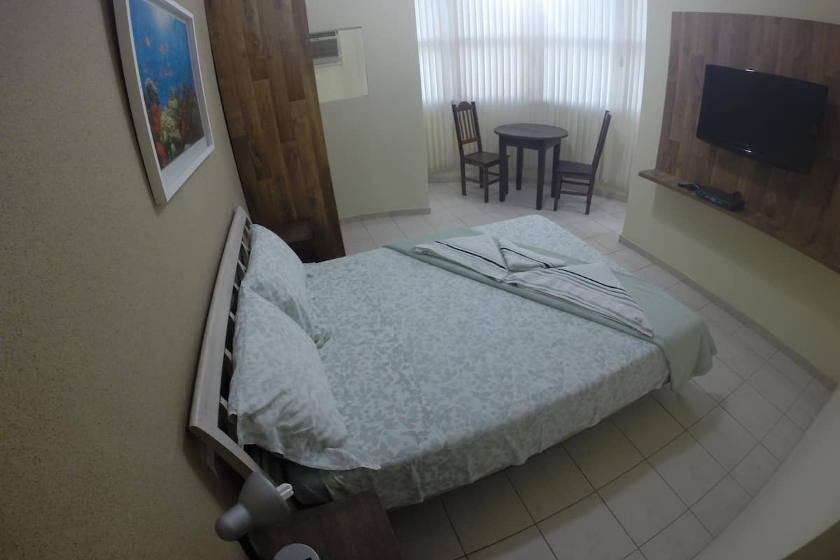 Ein Hotelzimmer mit Bett, Schreibtisch, Stuhl, Fernseher und einem Fenster mit Vorhängen.