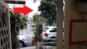 Ein schmaler Kopfsteinpflasterweg führt zu einem Hauseingang, während ein weißes Auto auf der Straße geparkt und ein roter Pfeil zum Eingang zeigt.