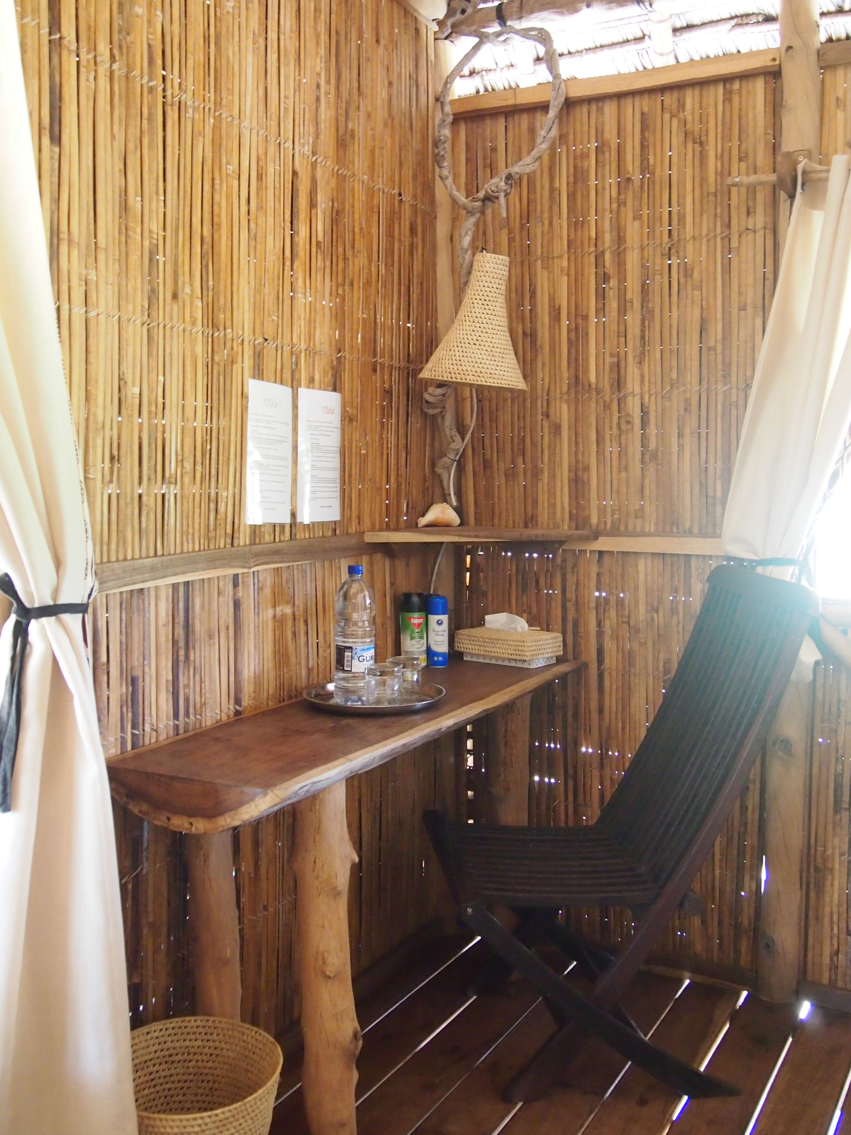 Una habitación rústica de madera con una mesa, una silla, una lámpara colgante y un pequeño estante con objetos.