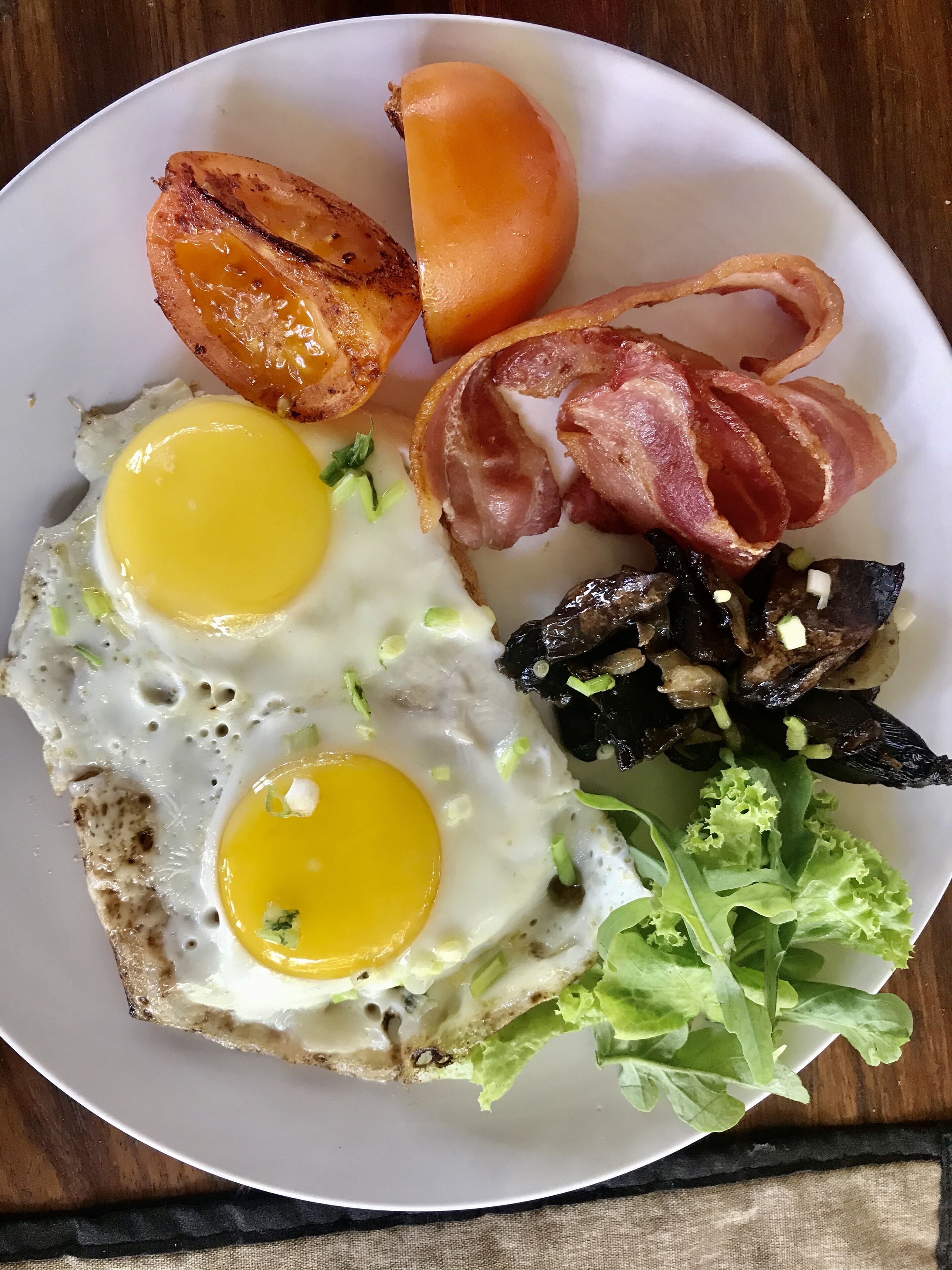 Um prato com ovos, bacon, batatas assadas e uma fatia de torrada.