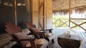 Een houten terras met twee houten stoelen en een tafel, bamboe wanden en een rieten dak.