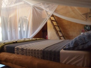 Una cama con dosel, una escalera y un ventilador en una habitación con techo de madera.