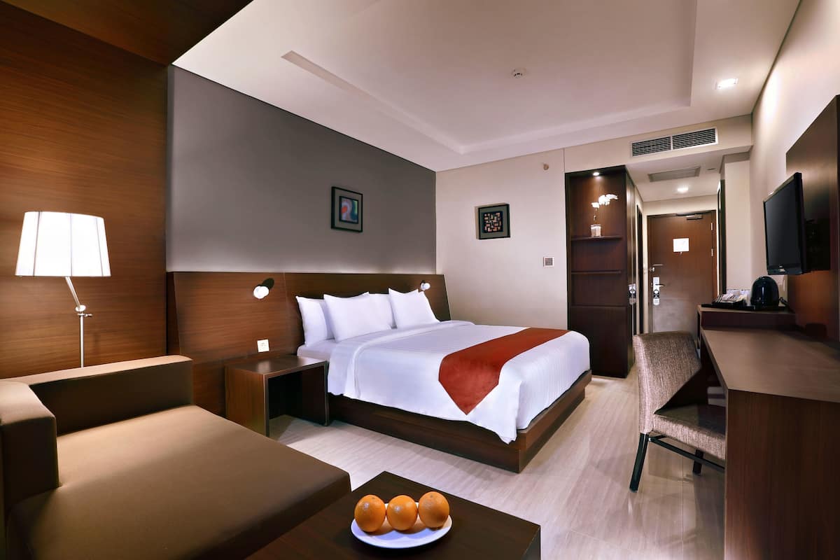 Une chambre d’hôtel avec un lit, une table de chevet, une lampe, une chaise et une petite table sur laquelle se trouvent des oranges.