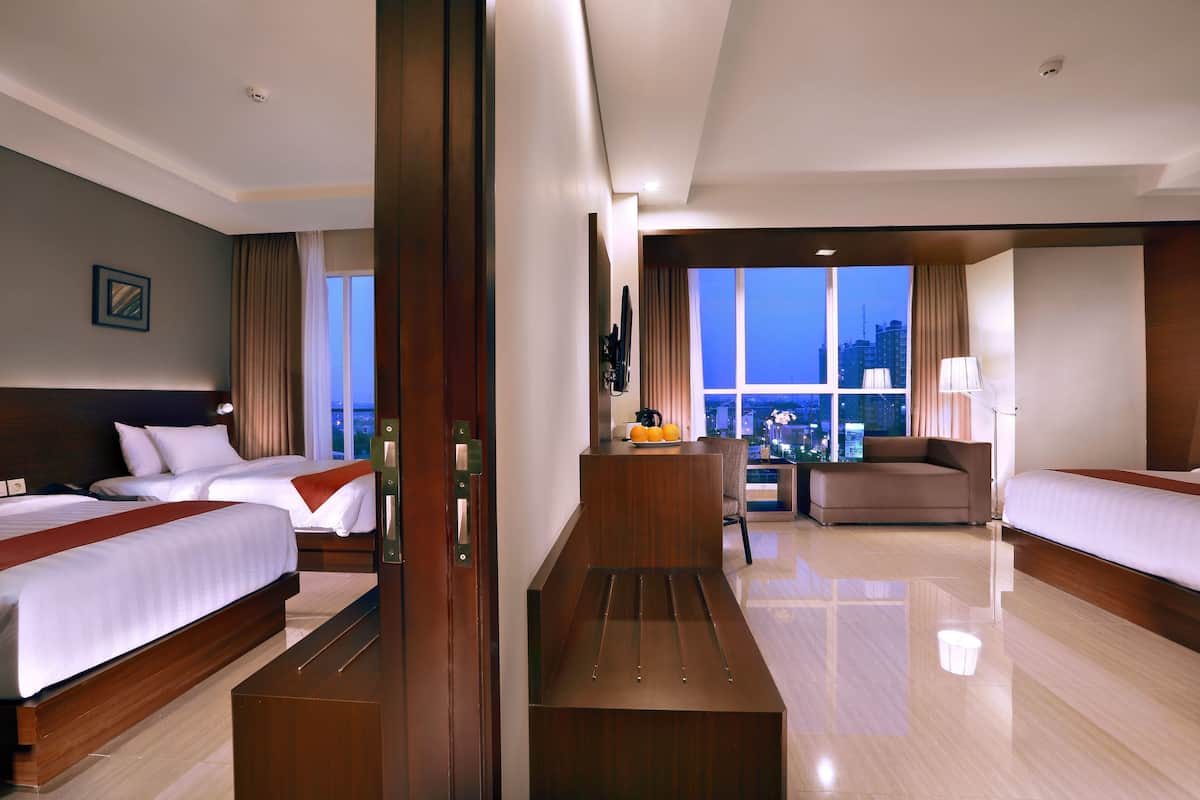Quarto de hotel com duas camas, um sofá, uma mesa de trabalho e uma janela grande com vista para a cidade.