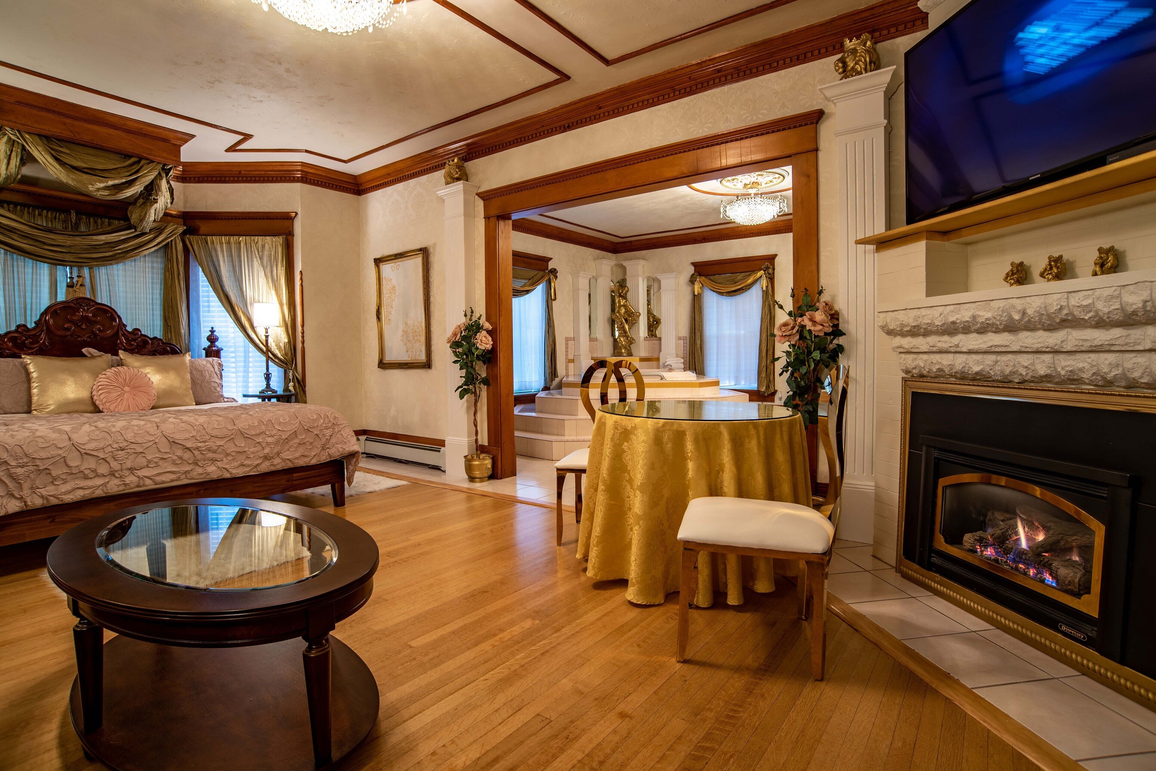 A spacious room with a large bed, a round table with chairs, a fireplace, and a television.