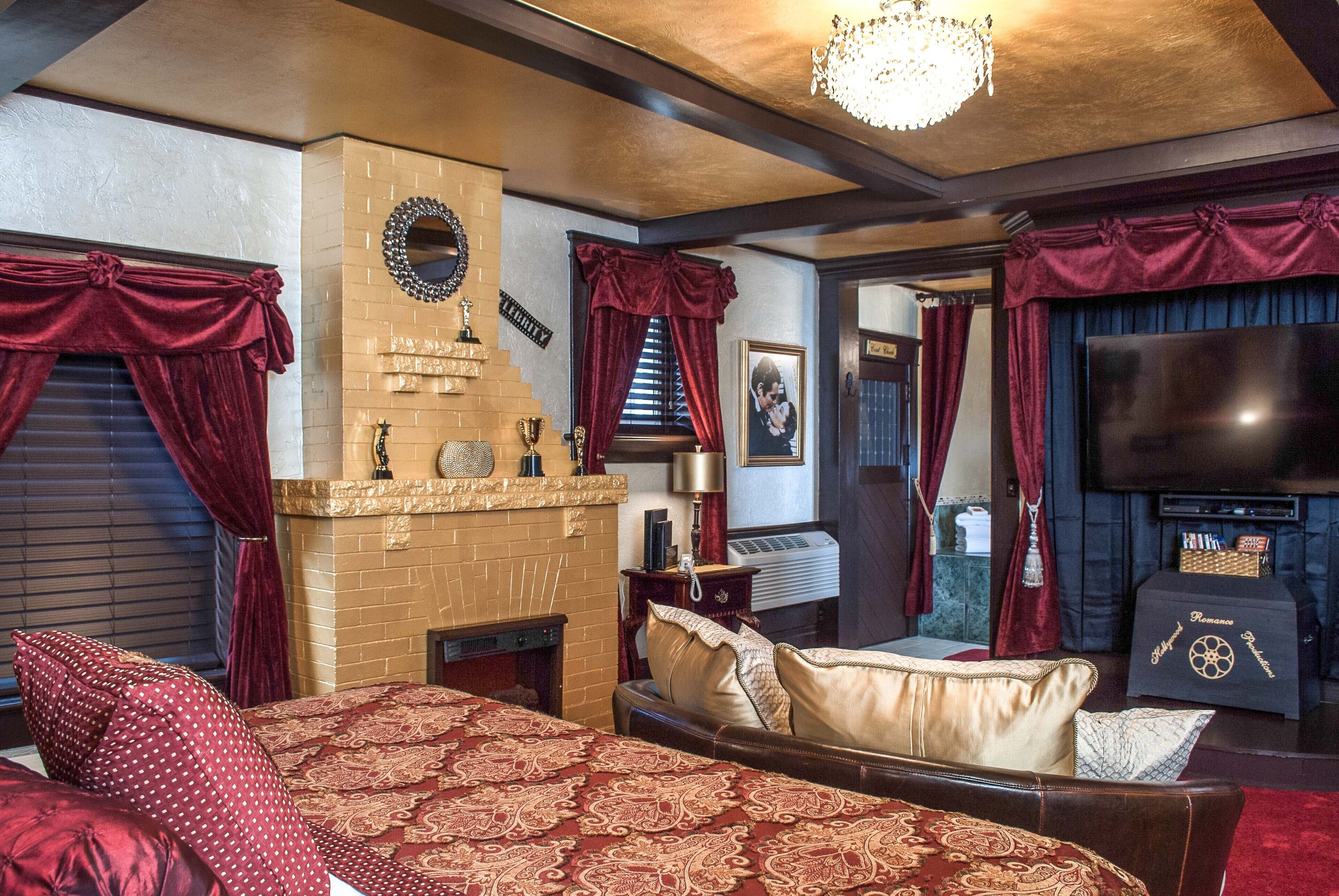 A hotel room with a large bed, a fireplace, a television, and a chandelier.