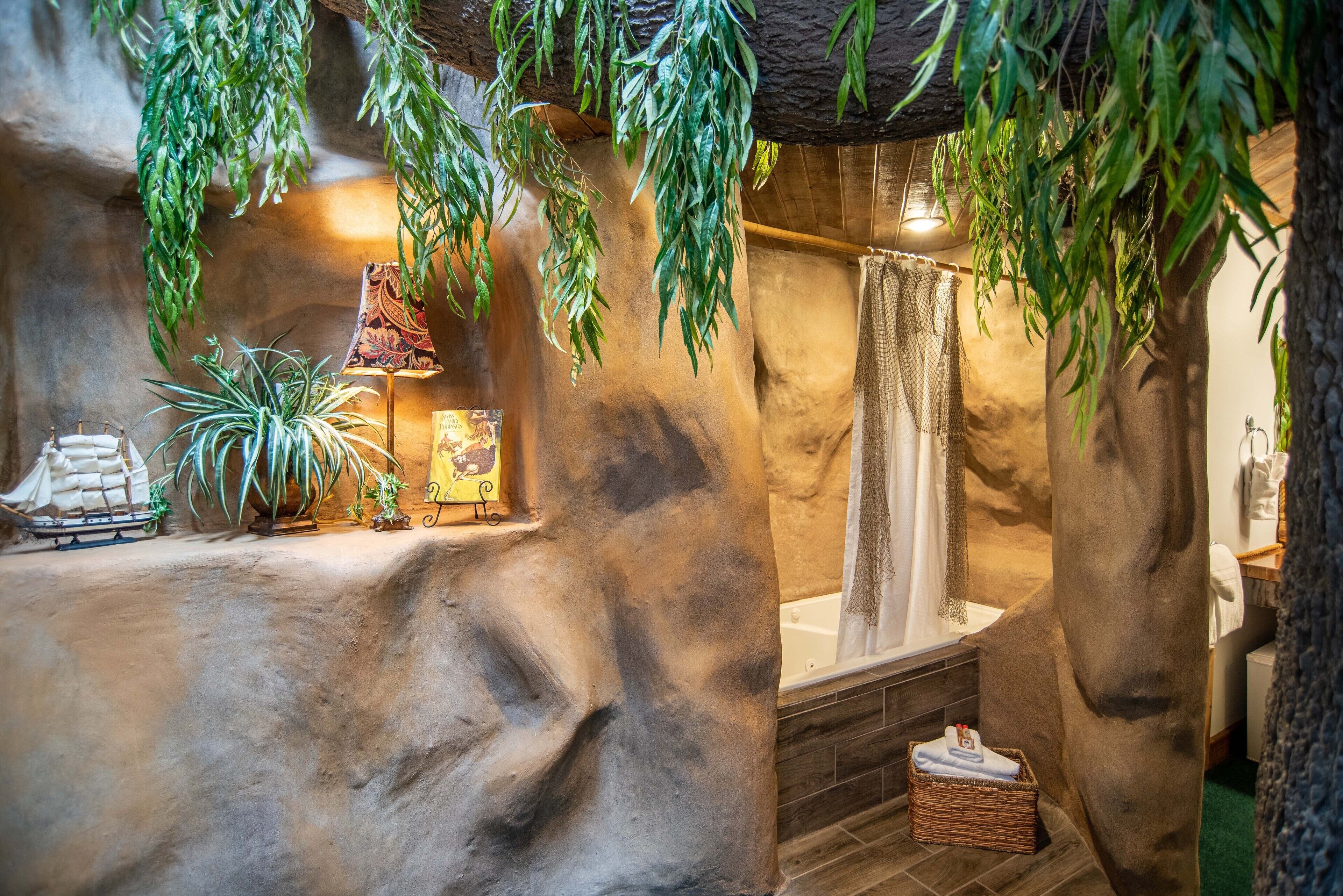 Un baño con pared de piedra, una bañera, plantas colgantes y un modelo de barco.