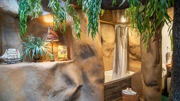 Un baño con pared de piedra, una bañera, plantas colgantes y un modelo de barco.