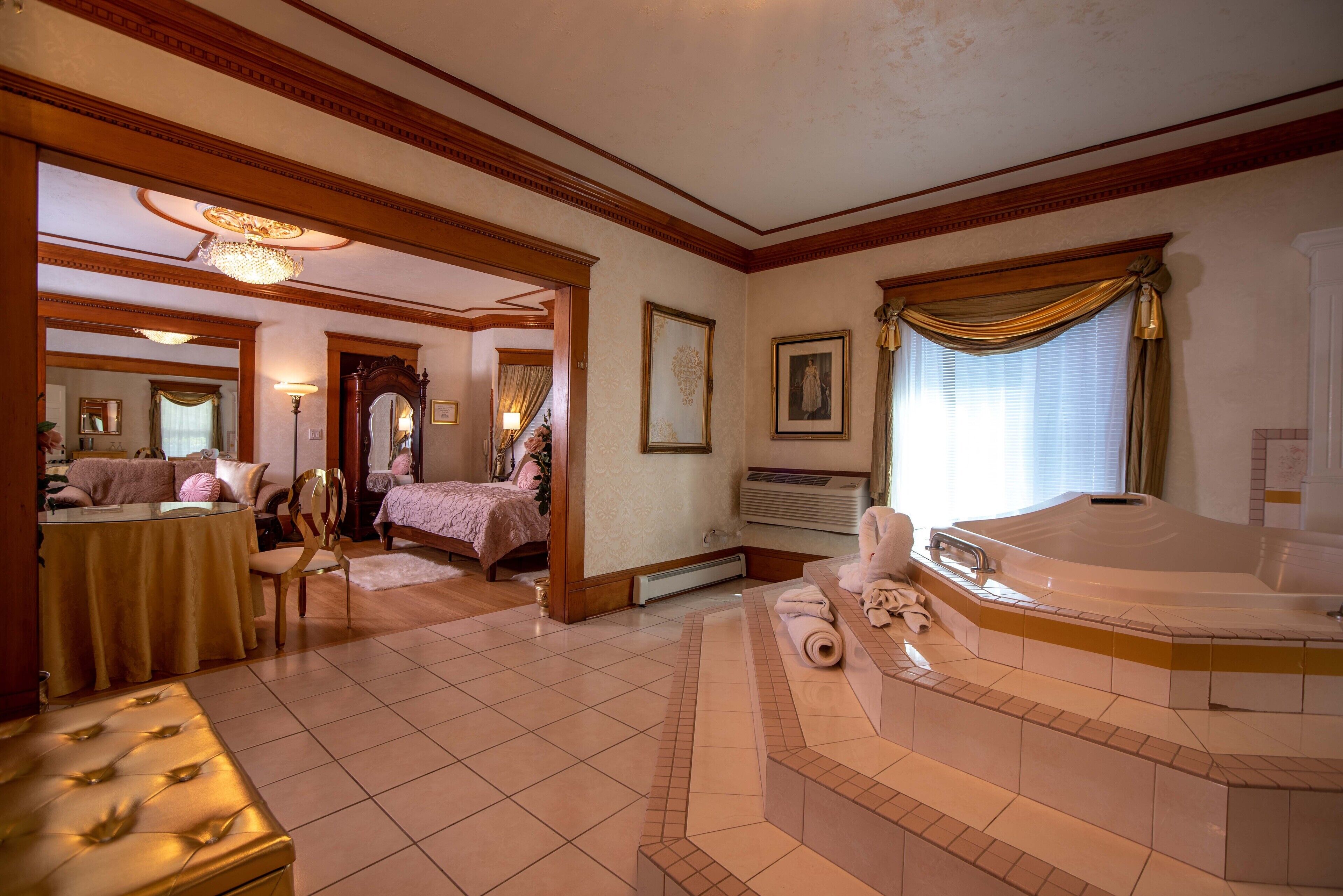 A spacious hotel room with a large bed, a sitting area with a table and chairs, a bathroom with a bathtub, and a dining area with a chandelier.