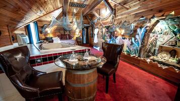 Interior rústico de cabaña con techo de madera, una mesa de vidrio con centro de mesa de vela, sillas de cuero, alfombra roja y un mural de un jardín de cactus.