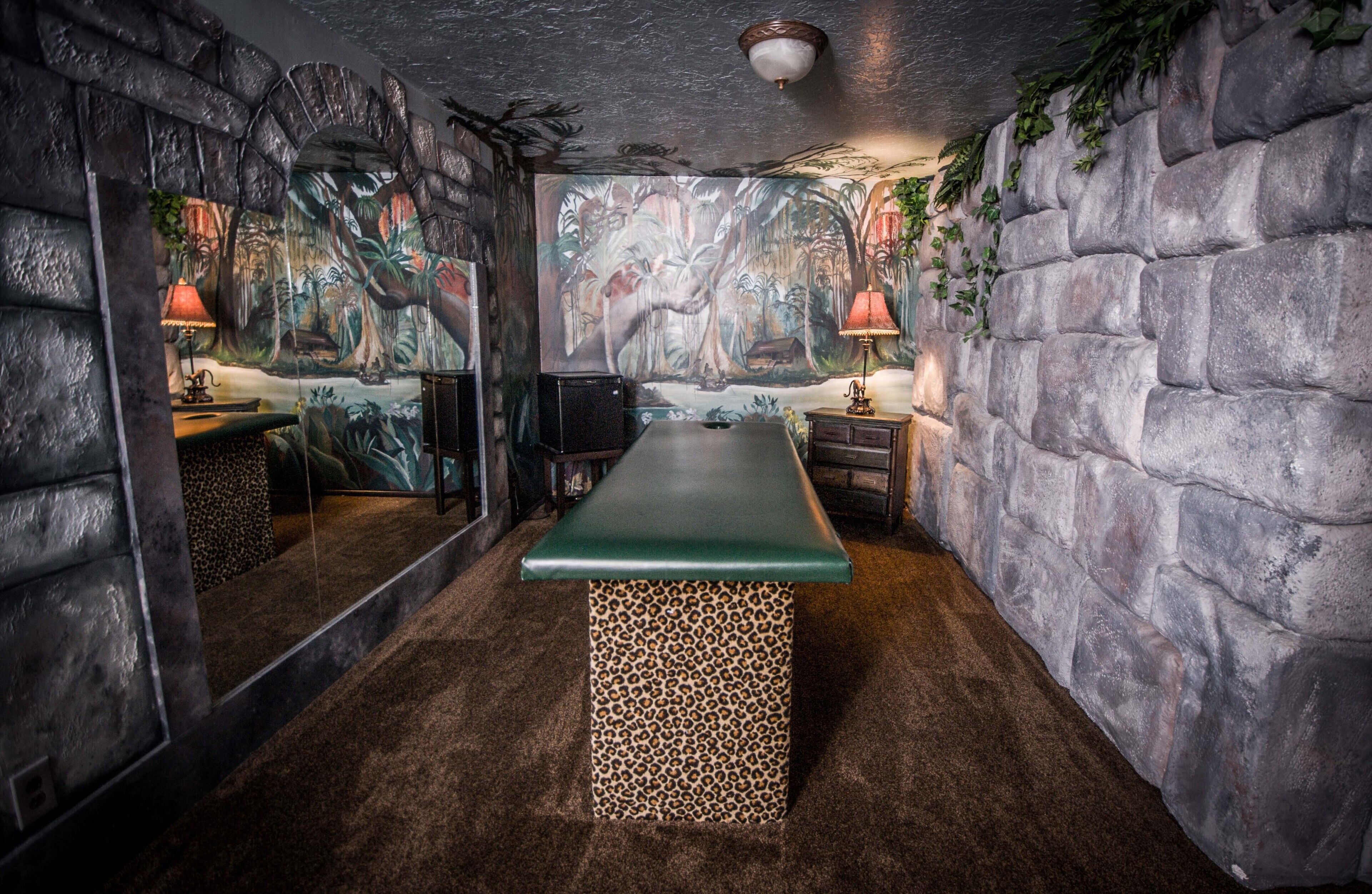 A room with a stone wall, a green bench, and a mural of a jungle scene.