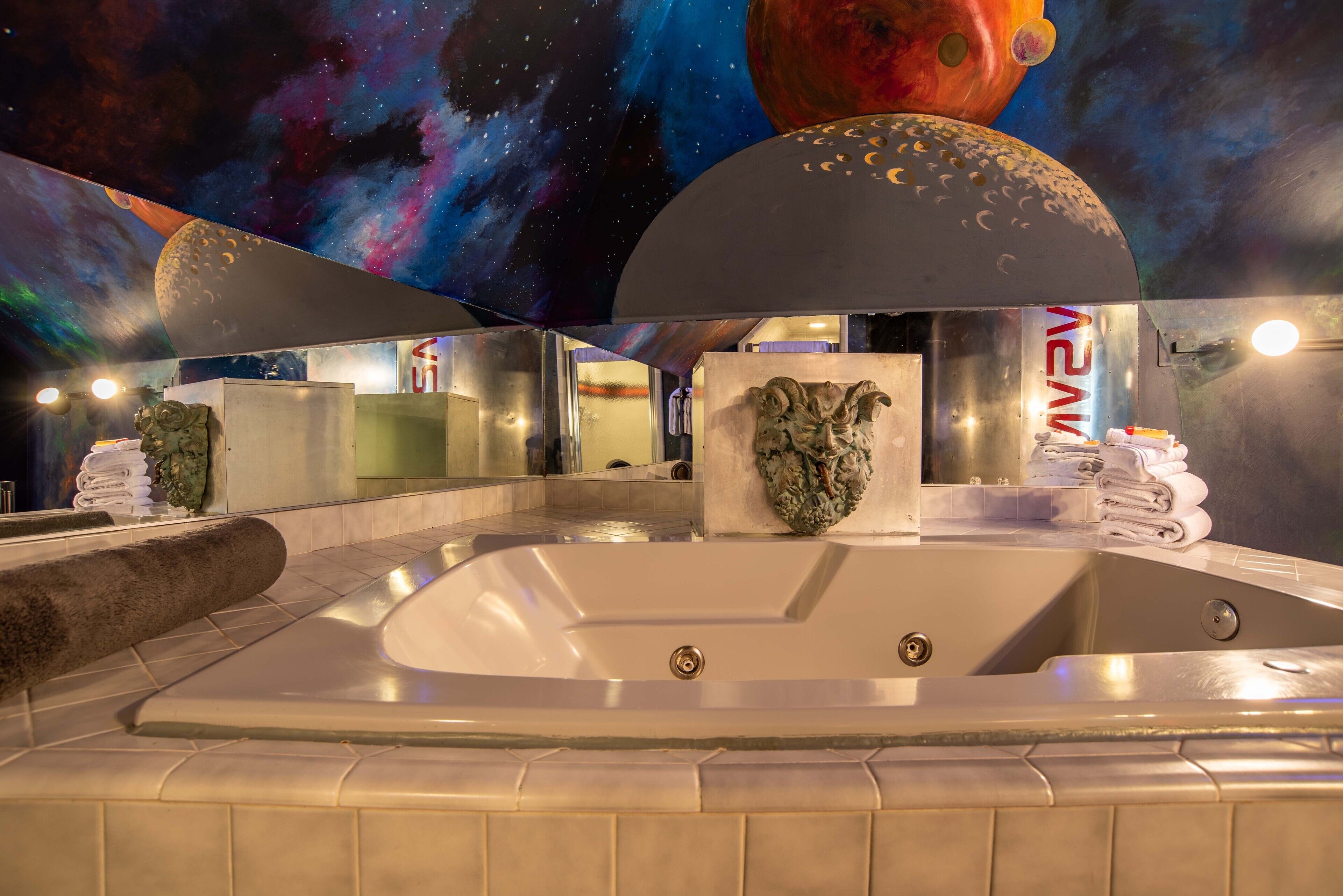 A spa area with a large hot tub, a mirror reflecting the room, and a space-themed mural on the ceiling.