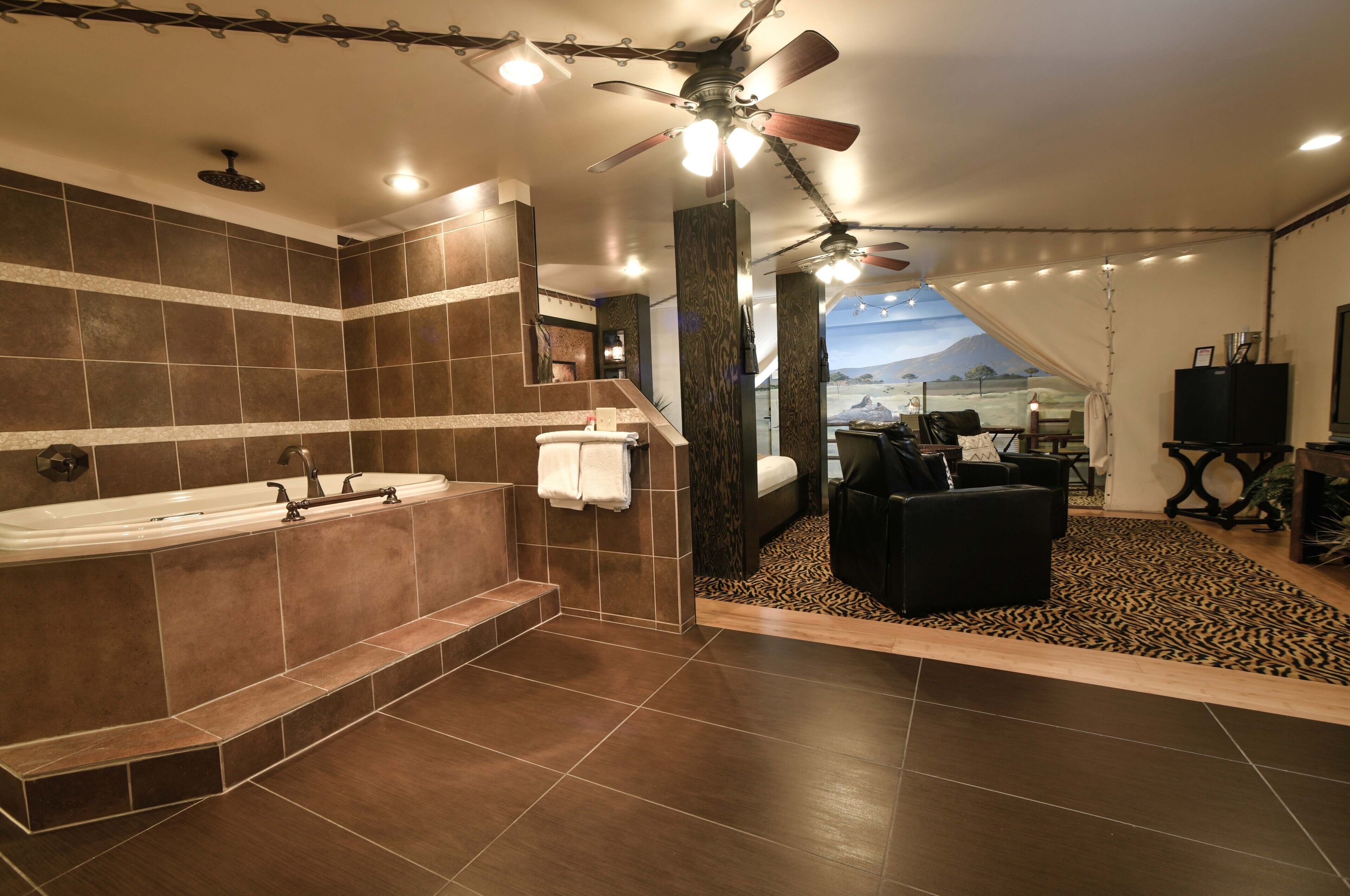Ein modernes Badezimmer mit einer großen Badewanne, einer Dusche und einem Deckenventilator. Man sieht einen Raum mit einem Sofa und einem Fernseher.