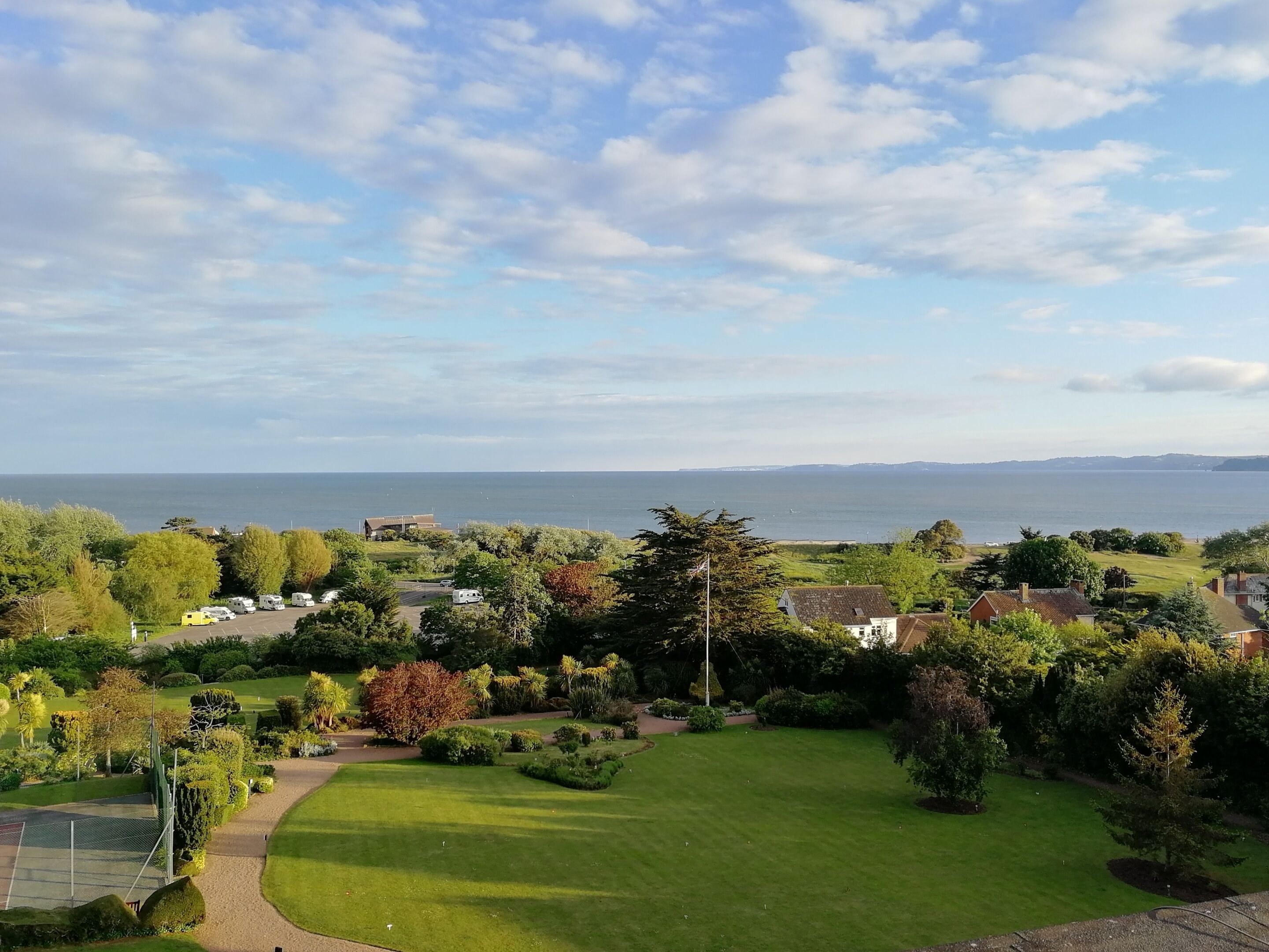A residential area with a view of the sea, houses, and a well-maintained lawn.