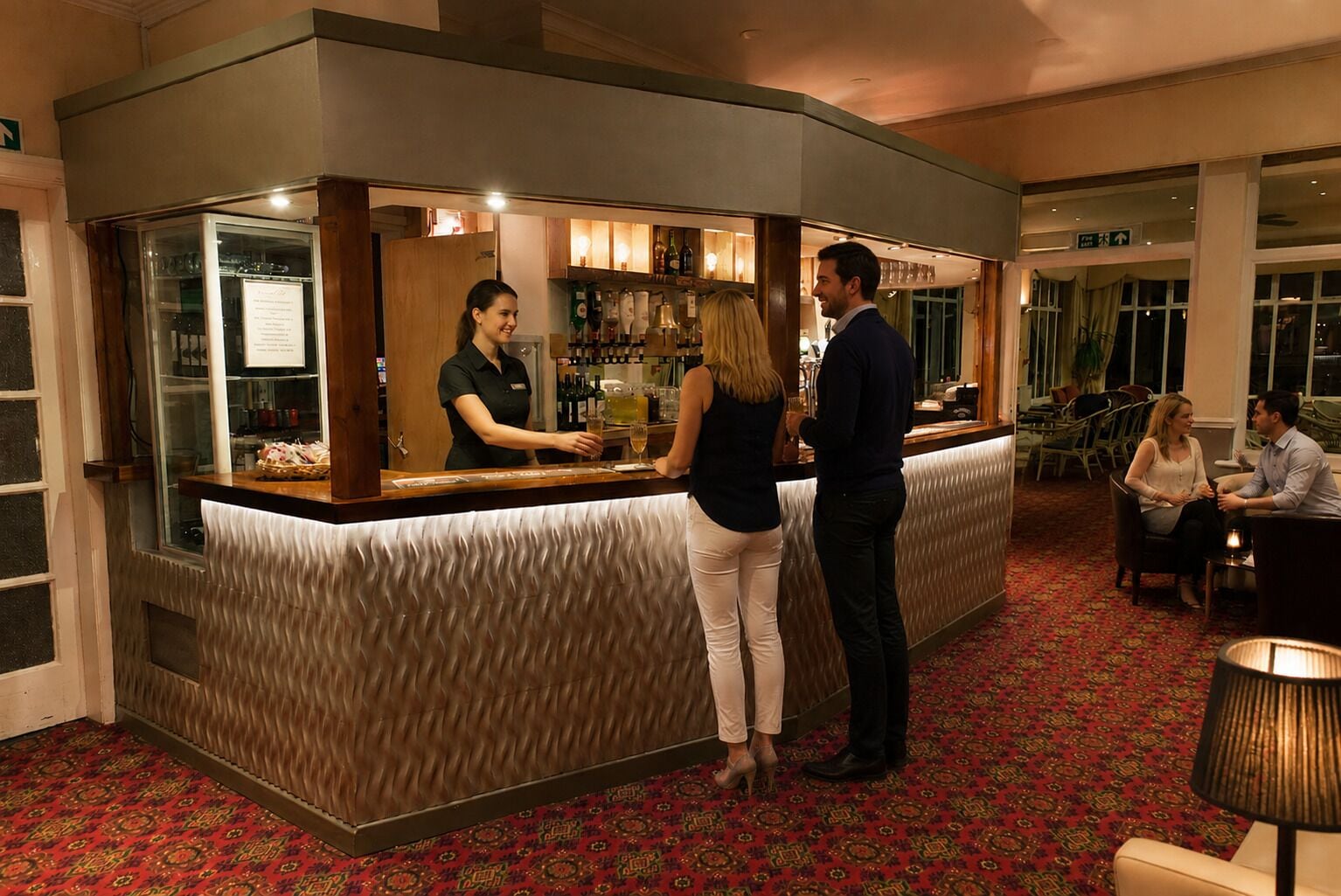 A bar area with a counter, a bartender, and a seating area with tables and chairs.