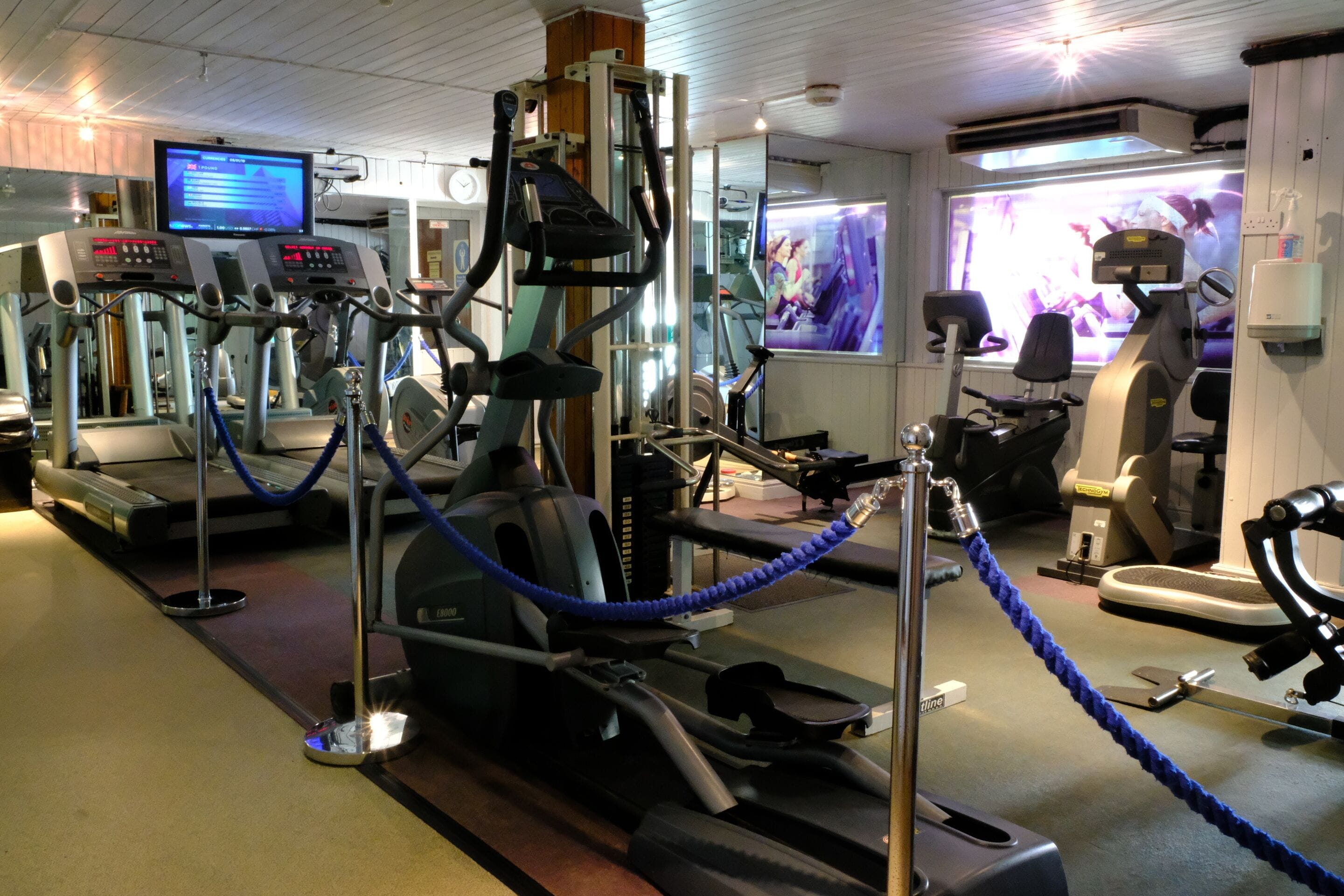 A gym with various exercise machines, a television, and a mirrored wall.