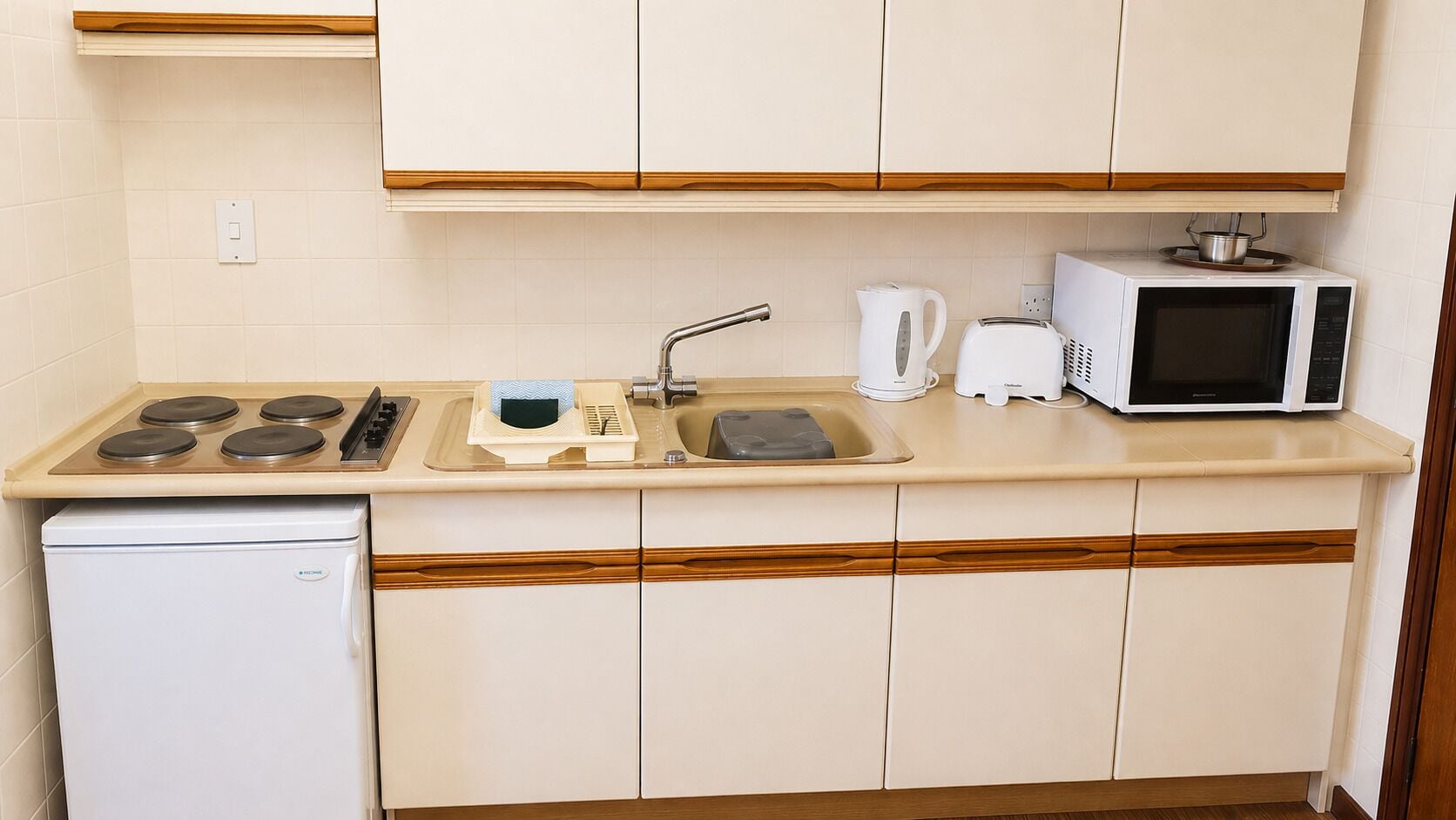 A compact kitchenette with a stove, sink, microwave, and a small refrigerator.
