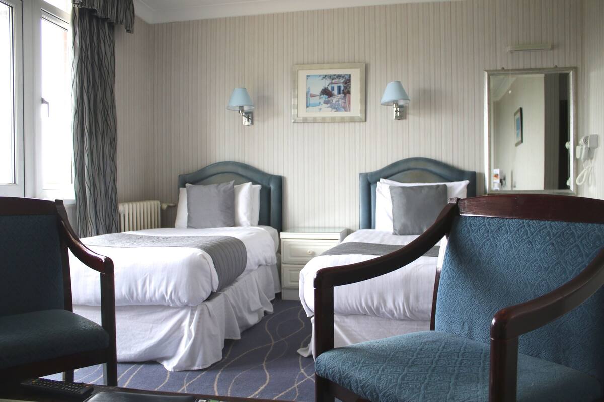 A hotel room with two beds, a chair, a desk, and a mirror.
