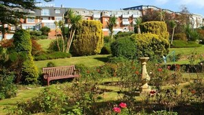 A well-maintained garden with a bench, a fountain, and neatly trimmed hedges.