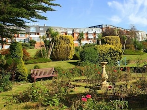 A well-maintained garden with a bench, a fountain, and neatly trimmed hedges. - The Devoncourt Resort (Exmouth)