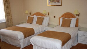 Two single beds with brown and white bedding, nightstands with lamps, and a window with curtains.
