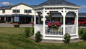 A gazebo with a white picket fence and a flower basket in the center, surrounded by a grassy area with small bushes. - WYE Motor Lodge Duncansville - Altoona (Hollidaysburg)