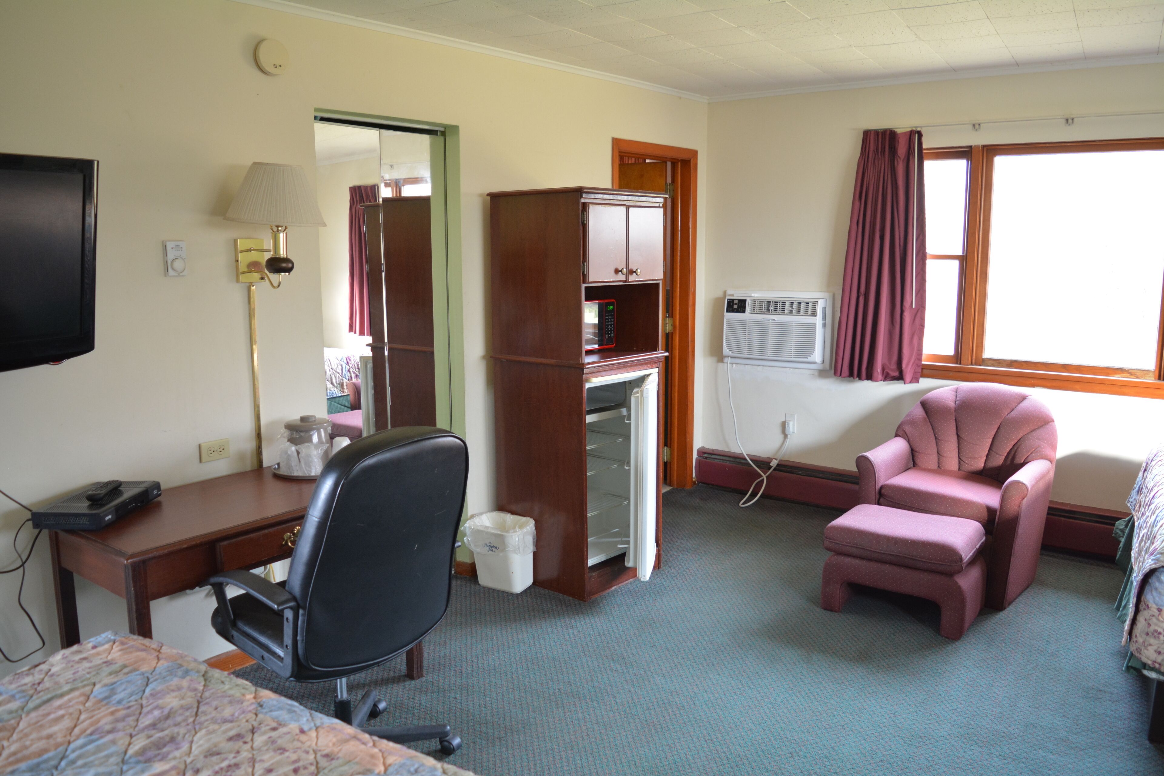 A hotel room with a bed, a desk, a chair, a minibar, a television, and a window with curtains.