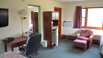 Et hotelværelse med seng, skrivebord, stol, minibar, fjernsyn og et vindue med gardiner.