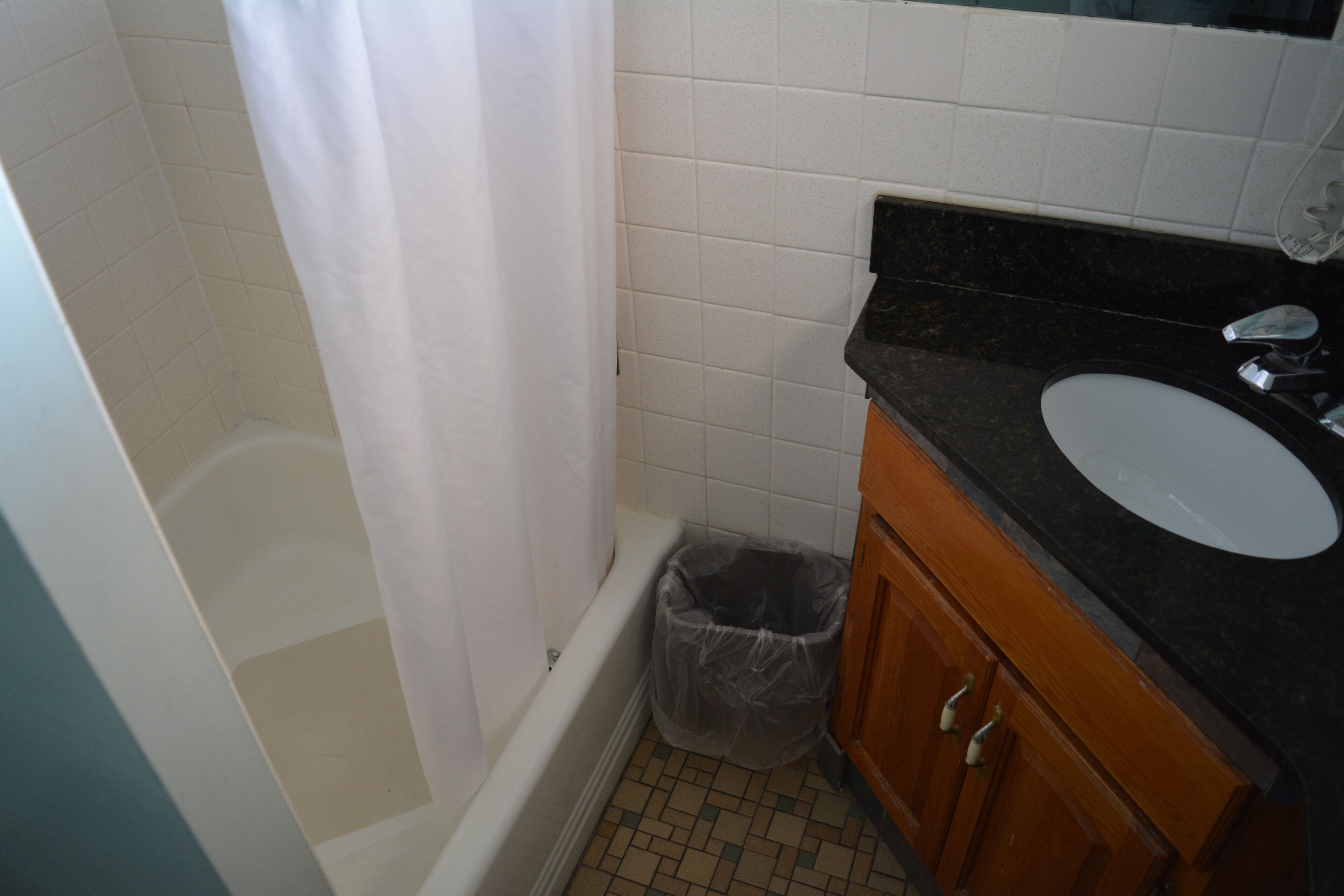 A bathroom with a bathtub, a white sink, and a trash can.