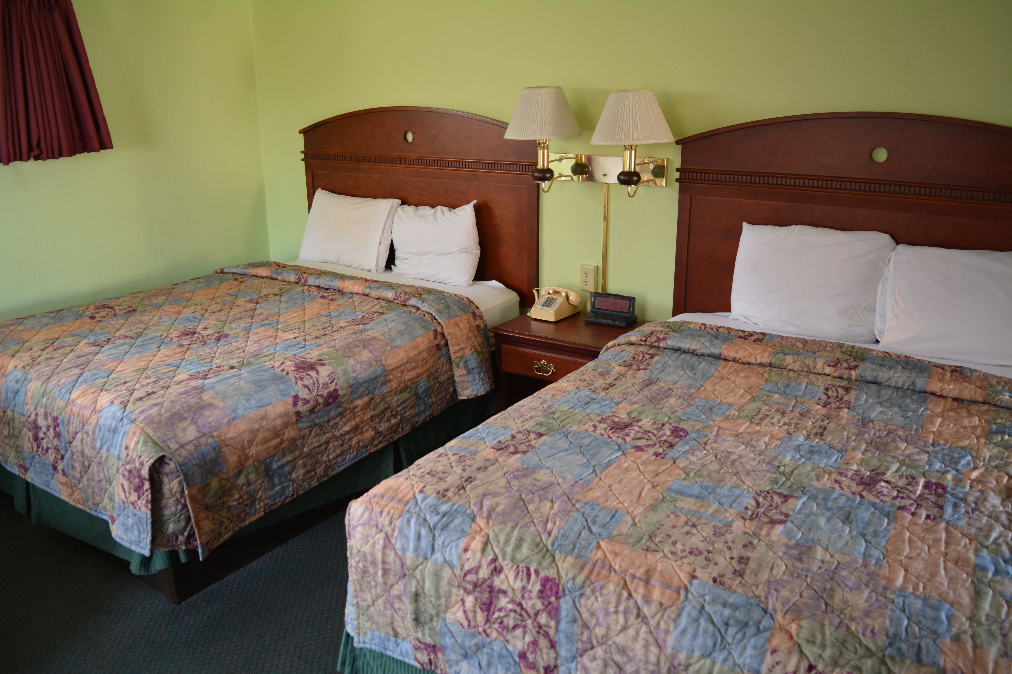 Habitación de hotel con dos camas, cada una con colcha de motivos florales, cabecero de madera y mesita de noche con lámpara y teléfono.