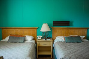 A hotel room with two beds, a nightstand with a lamp, a telephone, and a wall-mounted TV.