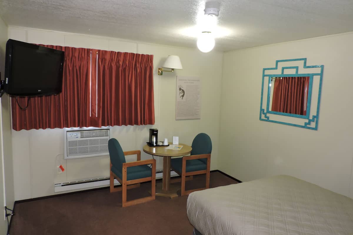 Een hotelkamer met een bed, een bureau met twee stoelen, een televisie, een kachel en een plafondlamp.