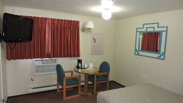 A hotel room with a bed, a desk with two chairs, a television, a heater, and a ceiling light.