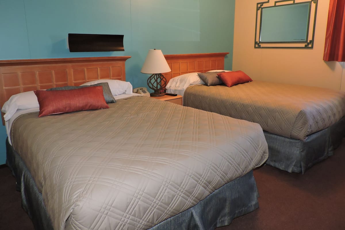 Een hotelkamer met twee bedden, een nachtkastje met een lamp, een telefoon en een spiegel aan de muur.