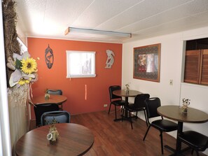 A dining area with wooden tables and chairs, a window with blinds, and decorative wall art.