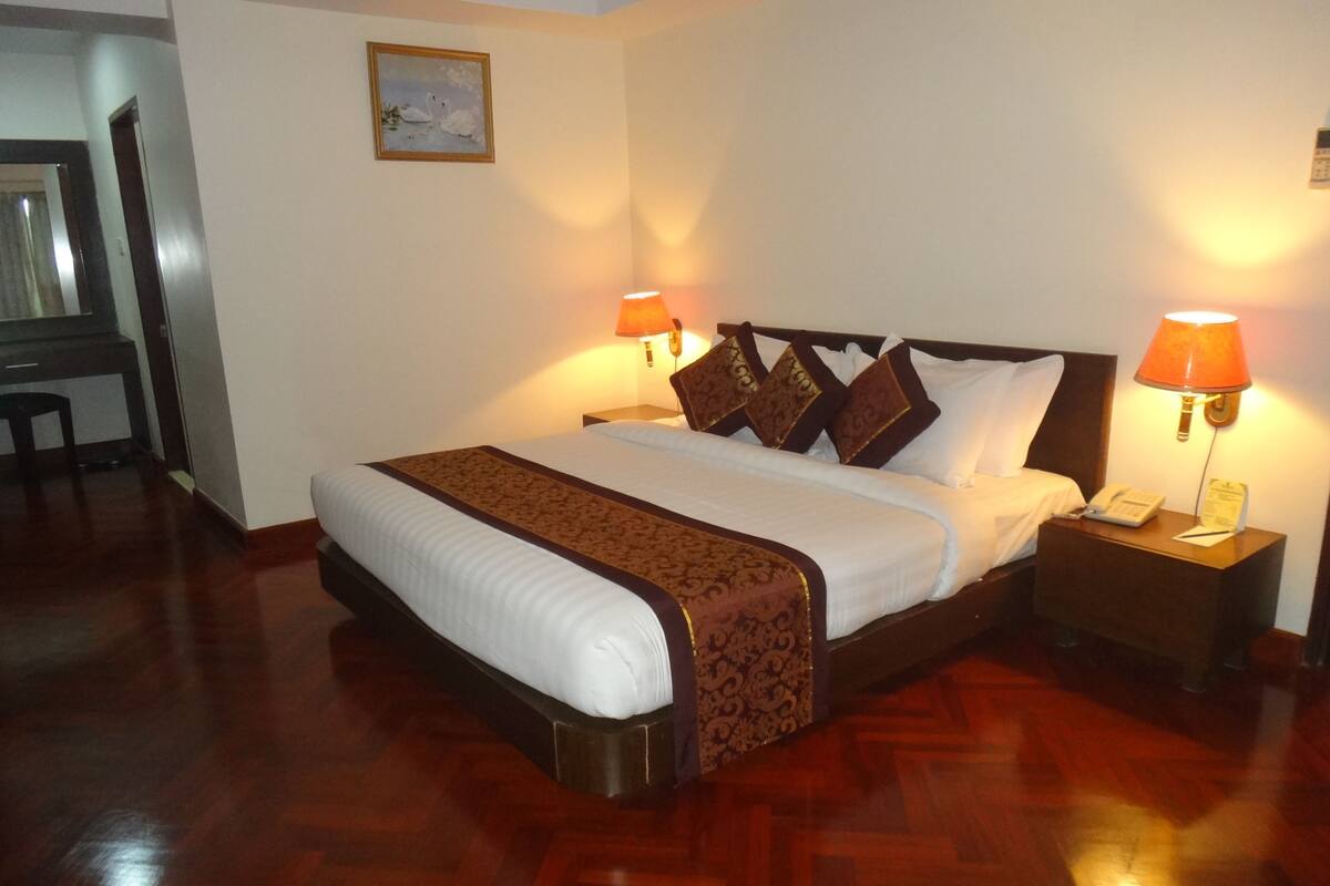 A hotel room with a large bed, two bedside lamps, a nightstand, and a wooden floor.