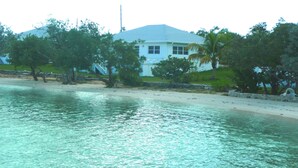 Una propiedad frente al mar con una casa blanca, aguas turquesas cristalinas y exuberante vegetación.