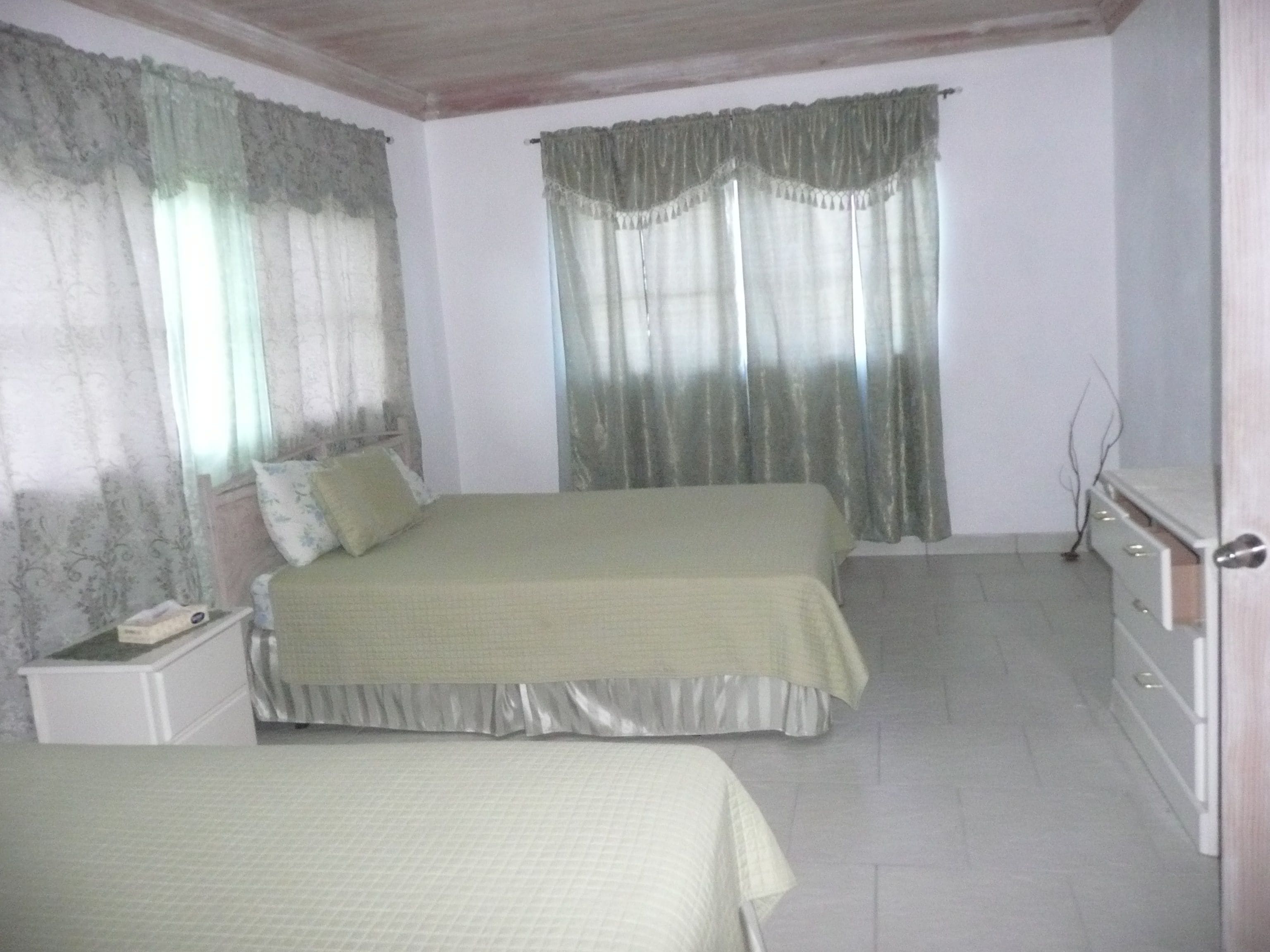 A bedroom with two beds, a nightstand, a dresser, and a window with curtains.