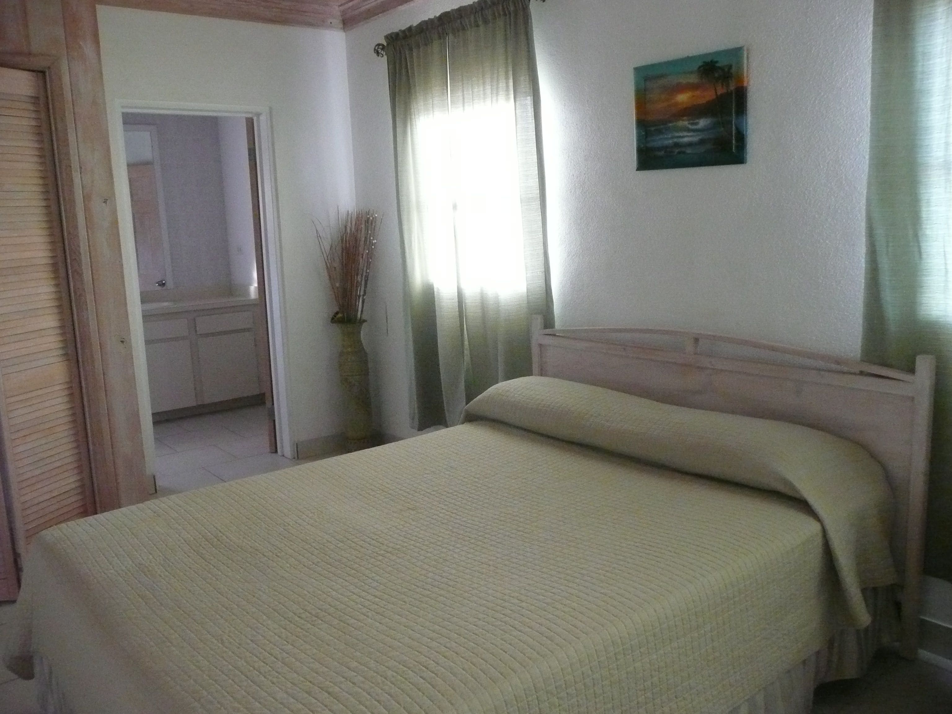 A bedroom with a bed, a painting on the wall, and a window with curtains.