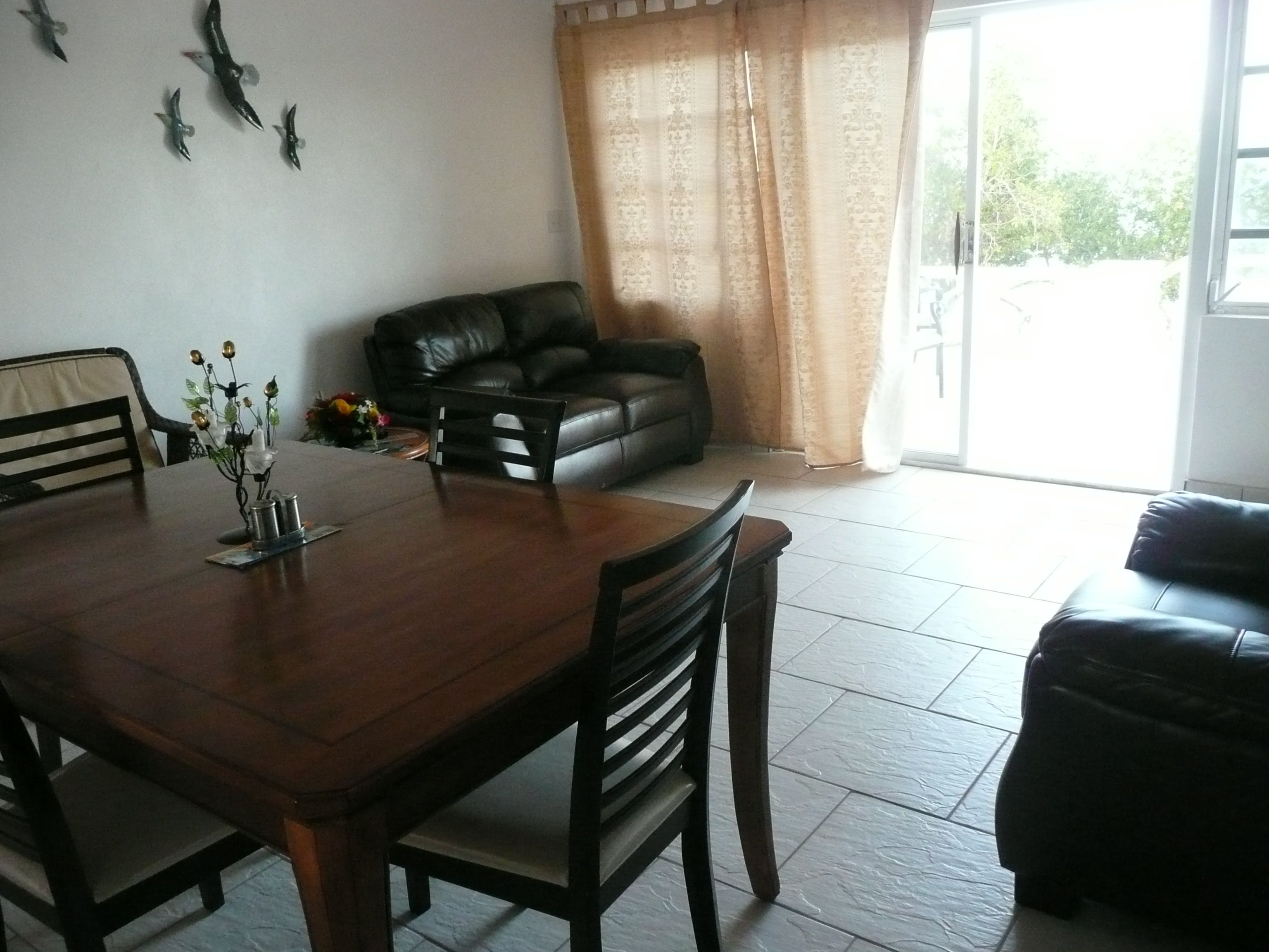 A dining area with a wooden table and chairs, a black leather sofa, and a dining table with a vase of flowers.