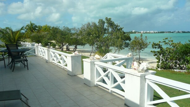 Un patio al aire libre con barandillas blancas, una mesa con sillas y vista a la playa y al océano.