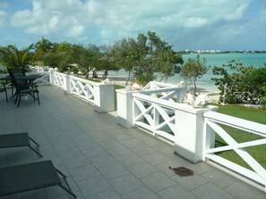 An outdoor patio with white railings, a table with chairs, and a view of the beach and ocean.